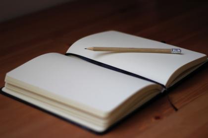 En uppslagen anteckningsbok och en penna illustrerar onlinekursen Skriv en roman på sex månader.